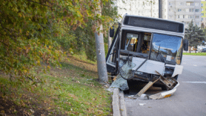 A white bus has crashed into a concrete utility pole beside a road, causing significant damage to the windshield and front bumper.