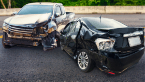 A silver pickup truck and a black sedan with visible damage are stopped on a paved road after a collision.