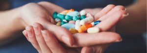 A person holds several assorted pills and capsules in their cupped hands.