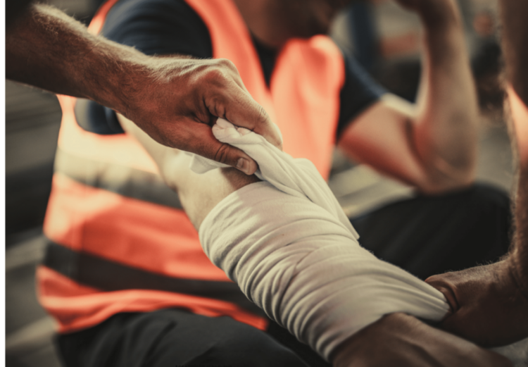 A person in a high-visibility vest wraps a bandage around another person's forearm.