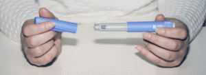 Person holding an insulin pen, with one hand removing the cap, over a white surface.