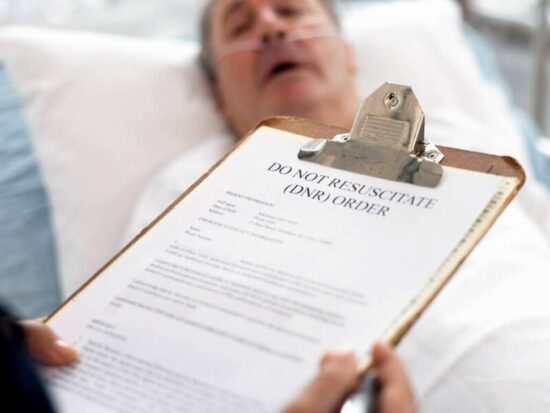 A patient lies in a hospital bed while a healthcare worker holds a clipboard displaying a Do Not Resuscitate (DNR) order form.