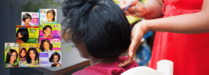 A person applies hair product to another person's hair. Boxes of various relaxer kits for textured hair are displayed on the left side of the image.