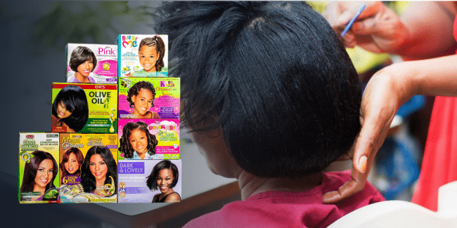 A person gets their hair styled while boxes of various hair relaxer products are shown in the foreground.