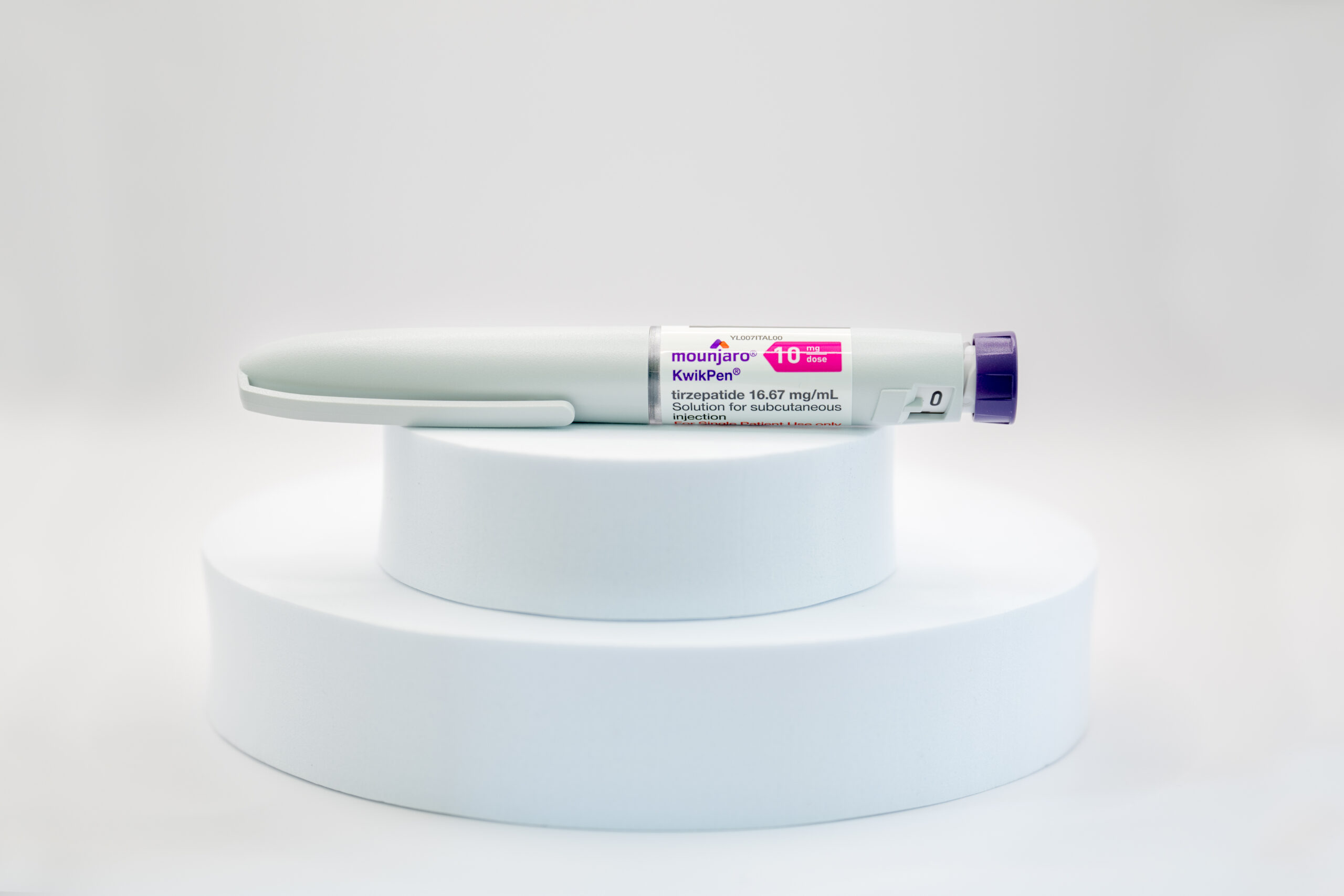 A Mounjaro KwikPen injection device is displayed horizontally on a white circular platform with a plain white background.
