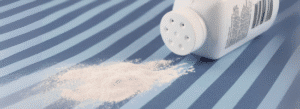 A white bottle of powder, tipped over, spills some white powder onto a blue striped surface.