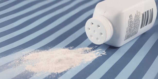 A white bottle of talcum powder lies on its side, dispensing powder onto a blue striped surface.