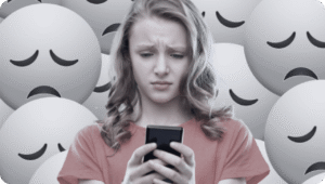 A young person looks concerned while reading a phone, with numerous sad face emojis in the background.