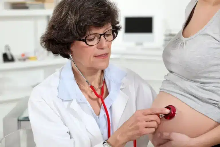 A doctor uses a stethoscope to listen to the abdomen of a pregnant person during a medical examination in a clinic.
