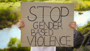 Person holding a cardboard sign reading "Stop Gender Based Violence" outdoors near water and greenery.