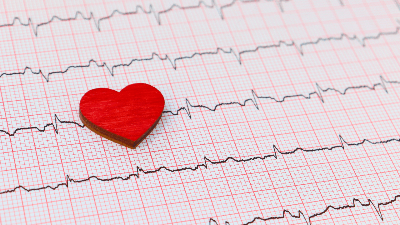 A small red heart shape placed on an electrocardiogram (ECG) printout with black heart rate lines on a grid background.